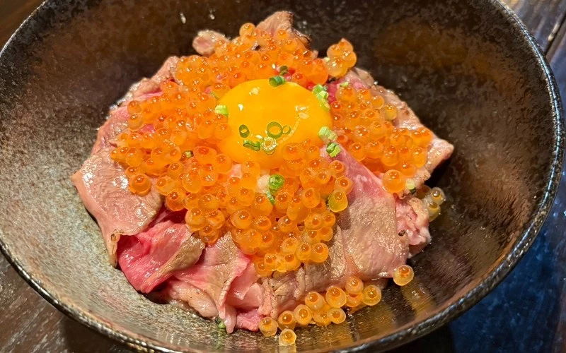 生牛肉片蓋飯，中央放生蛋黃，周圍鋪滿鮭魚卵