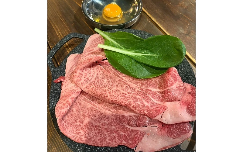生牛肉片擺放在黑色盤中，旁邊有菠菜葉與一顆蛋黃
