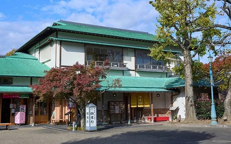 綠色屋頂的日式餐館外觀,前方有樹木與紅色長椅