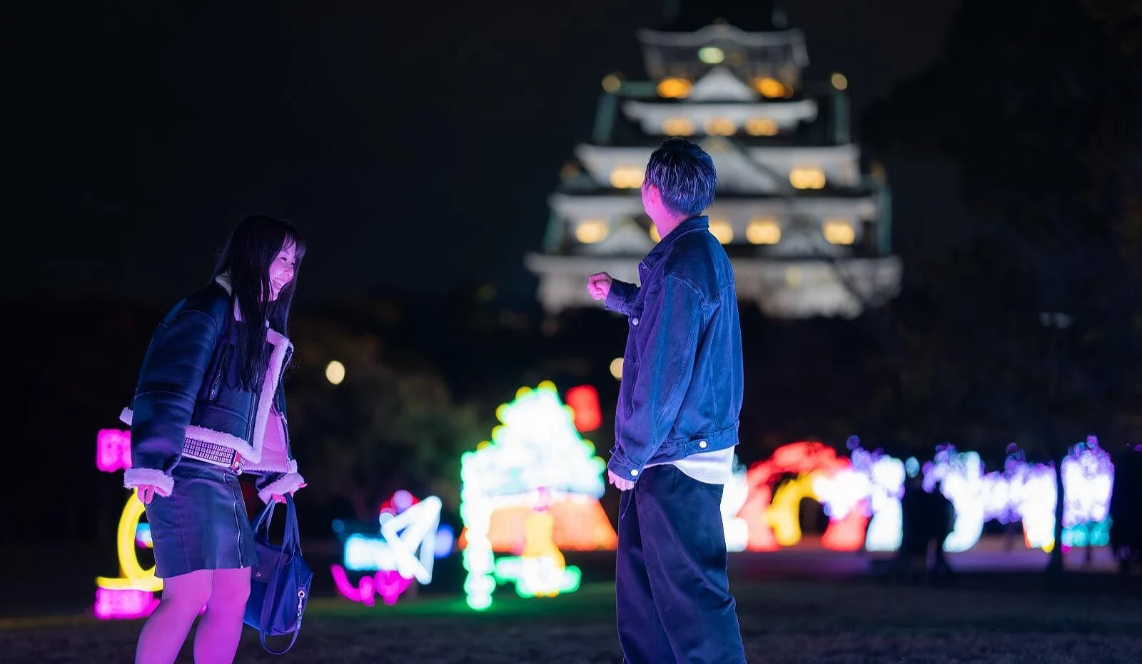 背景是入夜後點燈的大阪城,前景有一男一女在互動