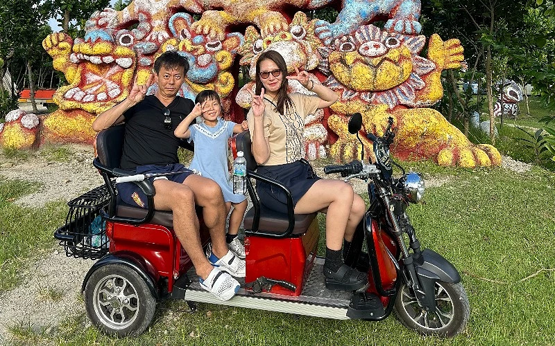 一家三口乘坐三輪車於黃色獅子前拍照