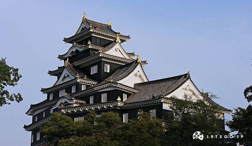 傳統日式城堡建築,黑白相間外牆搭配金色裝飾,前方有樹木