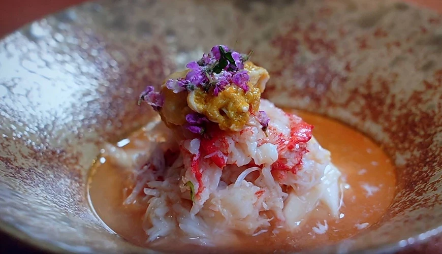 碗中盛放蟹肉料理,上方點綴紫色小花與黃色食材