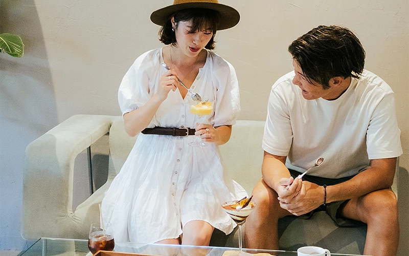 一位穿白洋裝的女子與一位白衣男子坐在沙發上享用甜點