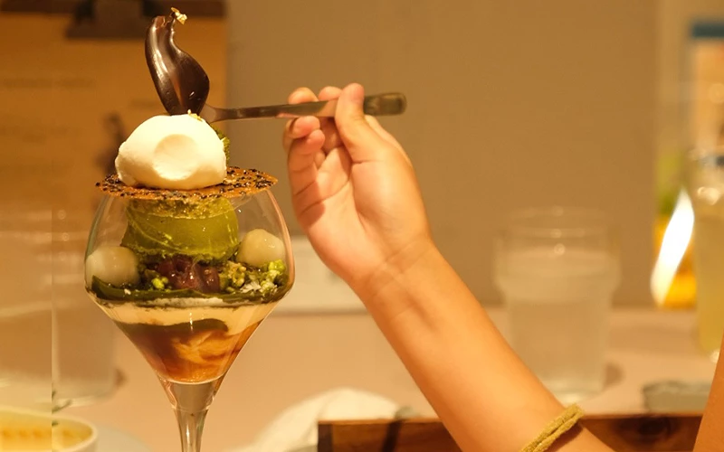 手持湯匙舀起一杯抹茶甜點，內含白玉與紅豆層次