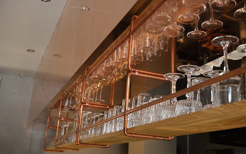 吧檯上方以銅管架懸掛整齊排列的酒杯與玻璃杯