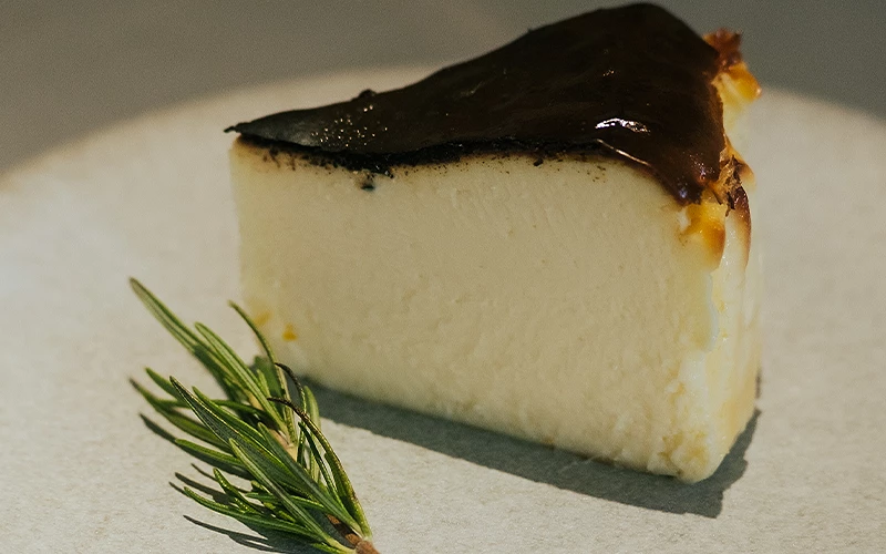 一片表面焦糖化的巴斯克乳酪蛋糕旁放有迷迭香枝