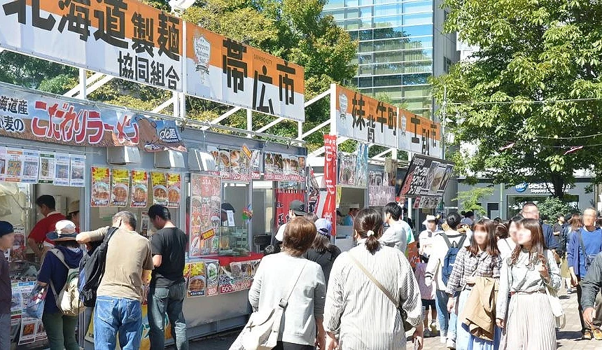 札幌大通公园秋季丰收祭现场,旅客穿梭于各地美食摊位间,品尝北海道各地特色料理的热闹景象