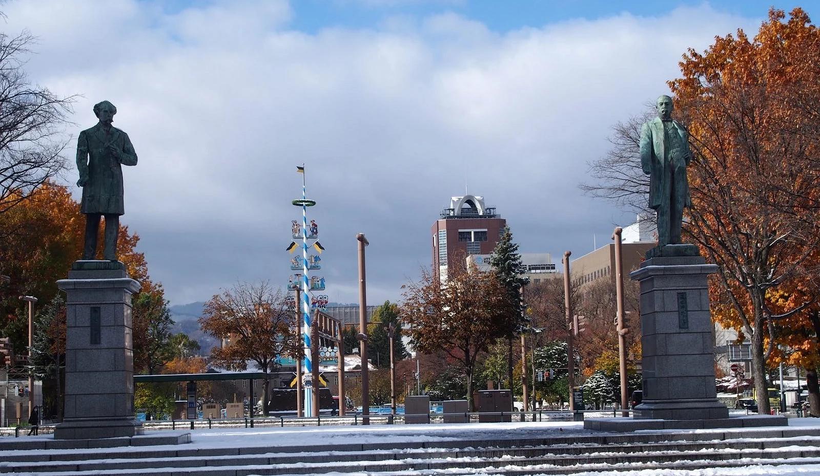 札幌大通公园历史文化区景象,前方为黑田清隆与贺莱斯・卡普朗铜像,后方可见蓝白相间的五月柱与秋季枫叶树林