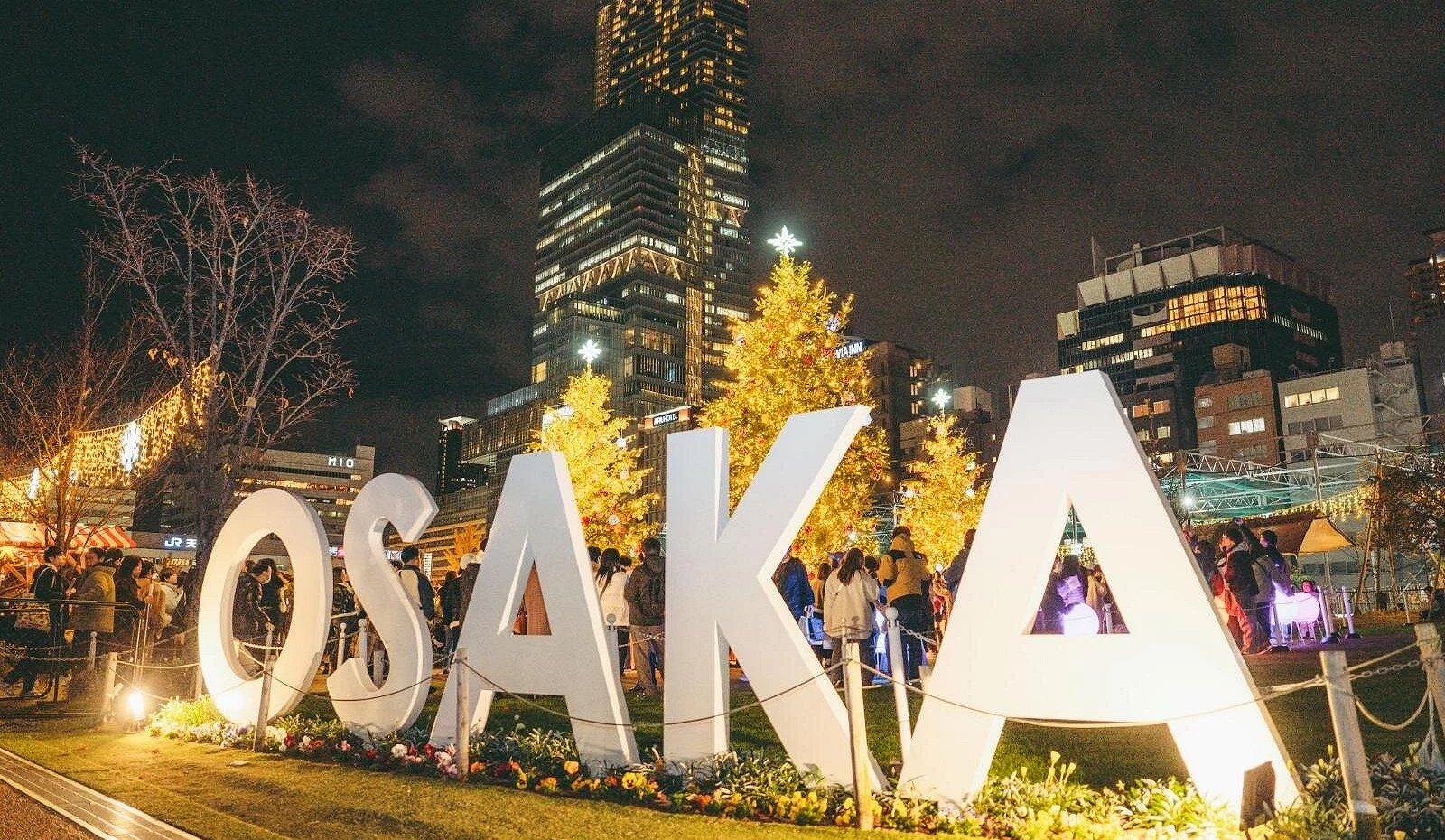 夜晚的天王寺公園「てんしば」前設有巨大白色「OSAKA」字樣裝置,背景為點亮的高樓與聖誕樹