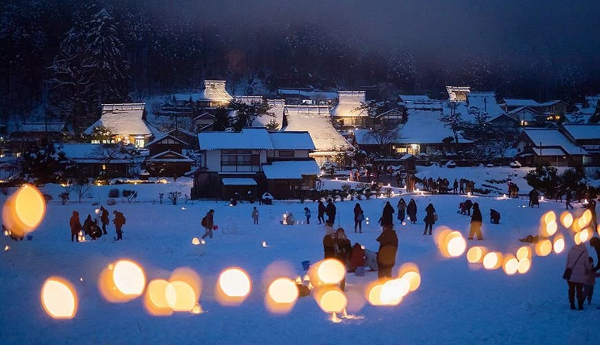 夜晚的美山茅葺之里雪燈廊活動現場,雪地上點滿燈籠,人們漫步其中,溫暖光影映照出夢幻的冬季景象