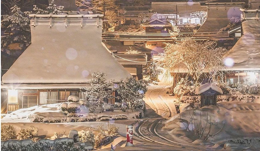 被厚雪覆蓋的美山茅葺之里,傳統茅草屋在燈光映照下閃爍著金色光芒