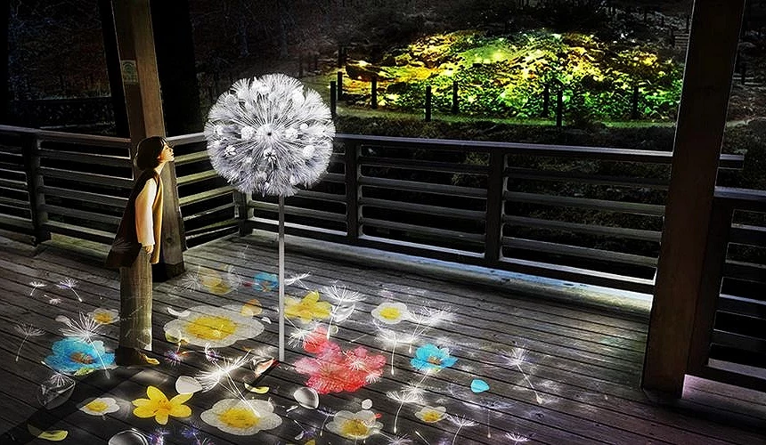 神戶六甲山夜間展覽「光之森」藝術裝置,一名女子凝望發光的巨大蒲公英燈,地面與遠方映出繽紛光影與花朵圖樣