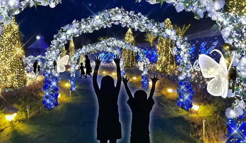夜晚的ローザンベリー多和田花園內,藍白燈飾構成花卉拱門與聖誕樹裝飾,前景有孩童剪影舉手欣賞燈海與發光蝴蝶的夢幻景象
