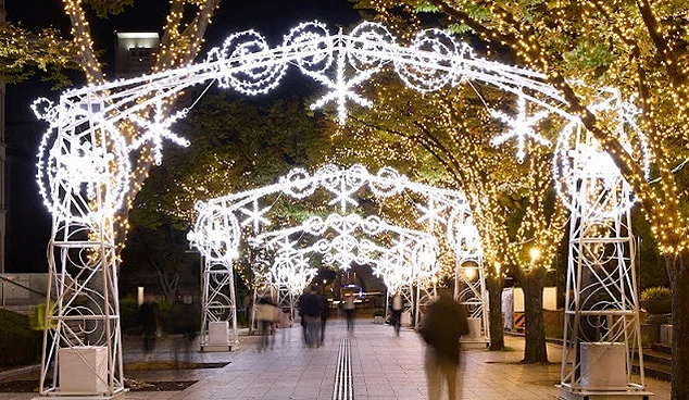 中之島步道上架設著雪花造型的白色光之拱門,兩側樹木閃爍著金黃燈串,遊客漫步其中,感受冬夜燈海的浪漫光影
