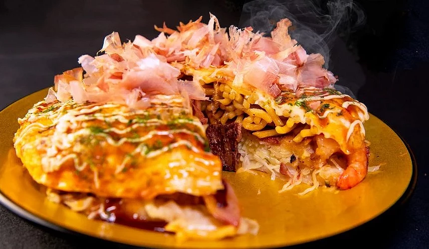 成田机场第三航厦「铁板烧 三本亭」的大阪烧料理,厚实面糊中夹有虾仁与培根,表面覆盖酱汁、美乃滋与柴鱼片