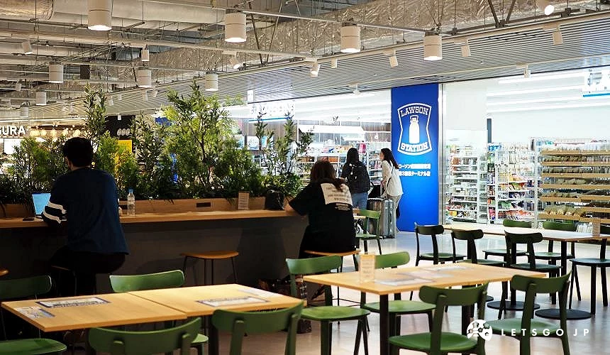 成田机场第三航厦2楼的美食与休憩空间,旅客在桌边休息或使用笔电,背景为 LAWSON 超商与「Fa-So-La KAGURA」商店入口