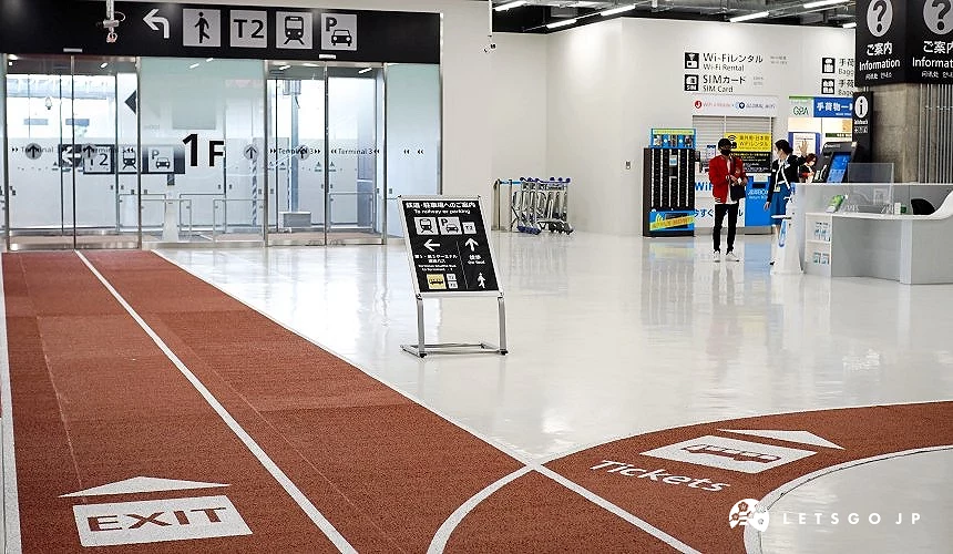 成田机场第三航厦1楼抵达大厅,红色地面导引线标示「EXIT」与「Tickets」方向,背景可见前往第二航厦及巴士的指标