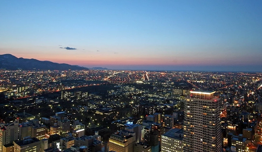 札幌JR塔展望室「T38」俯瞰夜景,夕阳余晖映照城市灯火,远方可见连绵山脉与小樽方向的海岸线