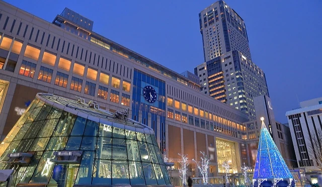 夜晚的札幌车站南口外观与JR塔,前方点亮蓝色圣诞树与玻璃圆顶入口