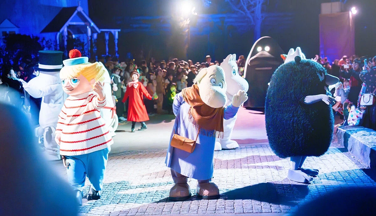 噜噜米公园夜间游行活动中,姆明与朋友们穿着节日服装登场,向观众挥手致意