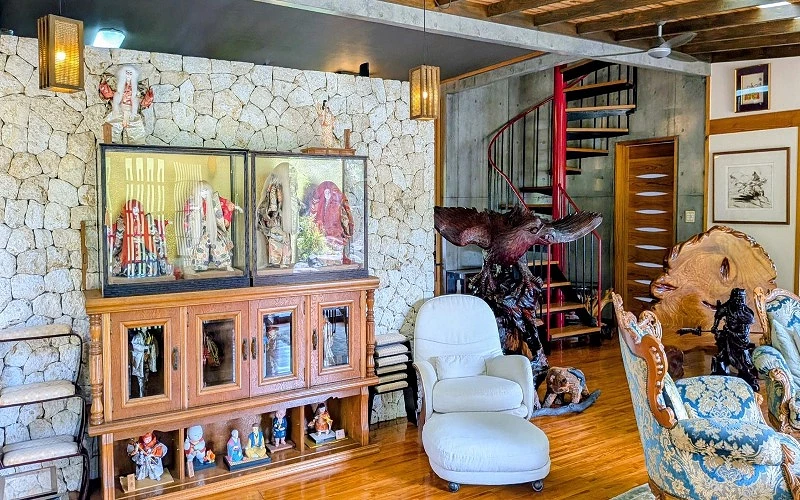 室內展示櫃中擺放日本人偶與雕刻作品，旁有白色椅子與木質地板