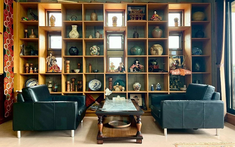 書架上整齊陳列陶瓷與人偶收藏，前方有黑色沙發與木質茶几