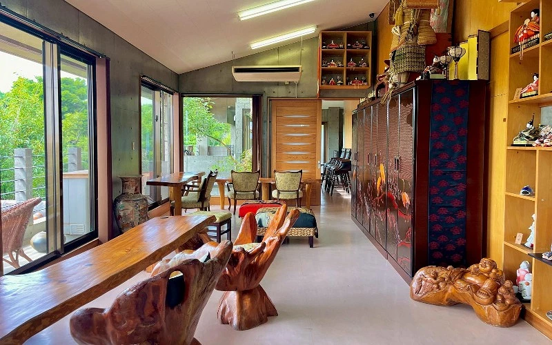 寬敞明亮的室內空間，擺放木質長桌與雕刻椅，牆上有人偶與收藏品