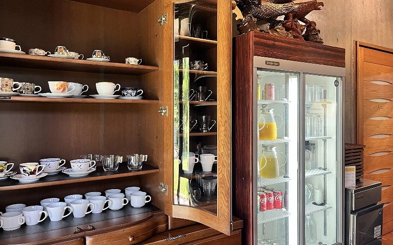 木質櫥櫃陳列多款咖啡杯與玻璃杯，旁邊是放有飲料的冰箱