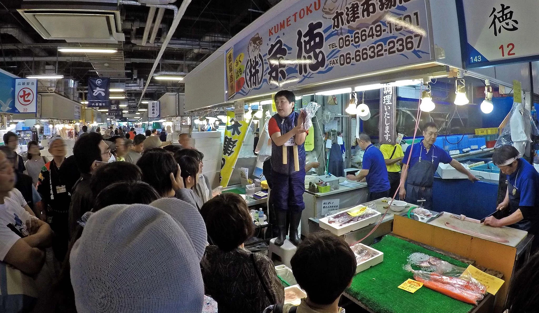 许多游客围在鱼市摊贩前,听摊贩老板介绍鱼类,并可能等待竞标