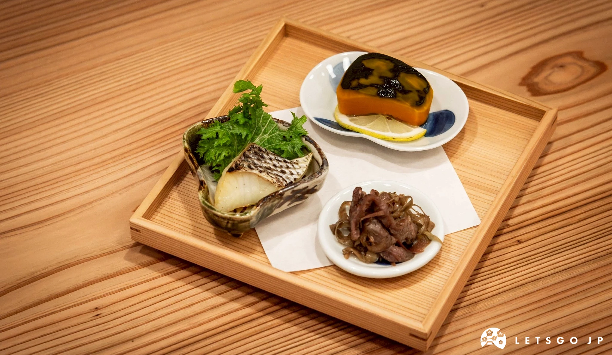 一組包含多道海鮮小菜的拼盤,食材可能包括鮑魚或貝類,擺放在木質托盤上,展現精緻的日式前菜組合。