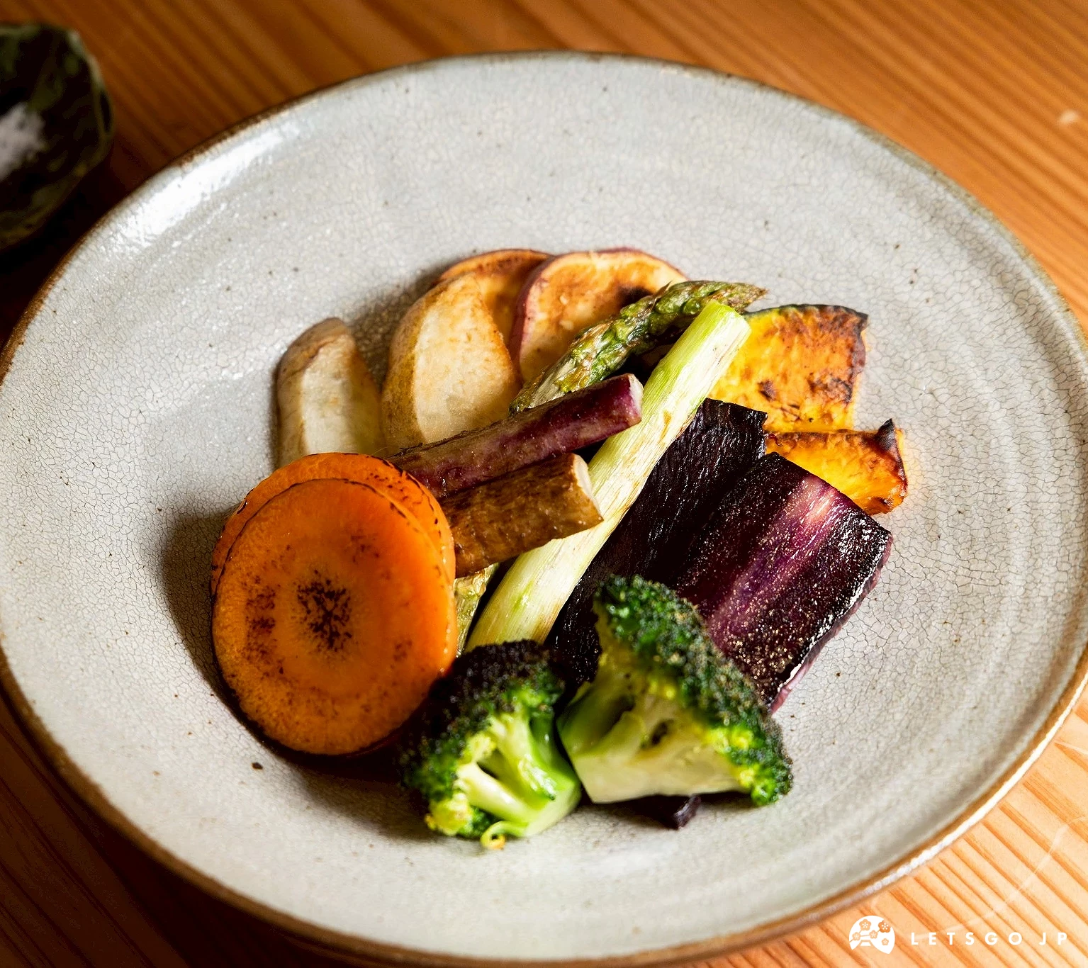 一份烤製或燉煮的季節蔬菜,色彩鮮豔,包括南瓜、茄子等,盛裝於白色圓盤中,展現料理的色彩平衡。