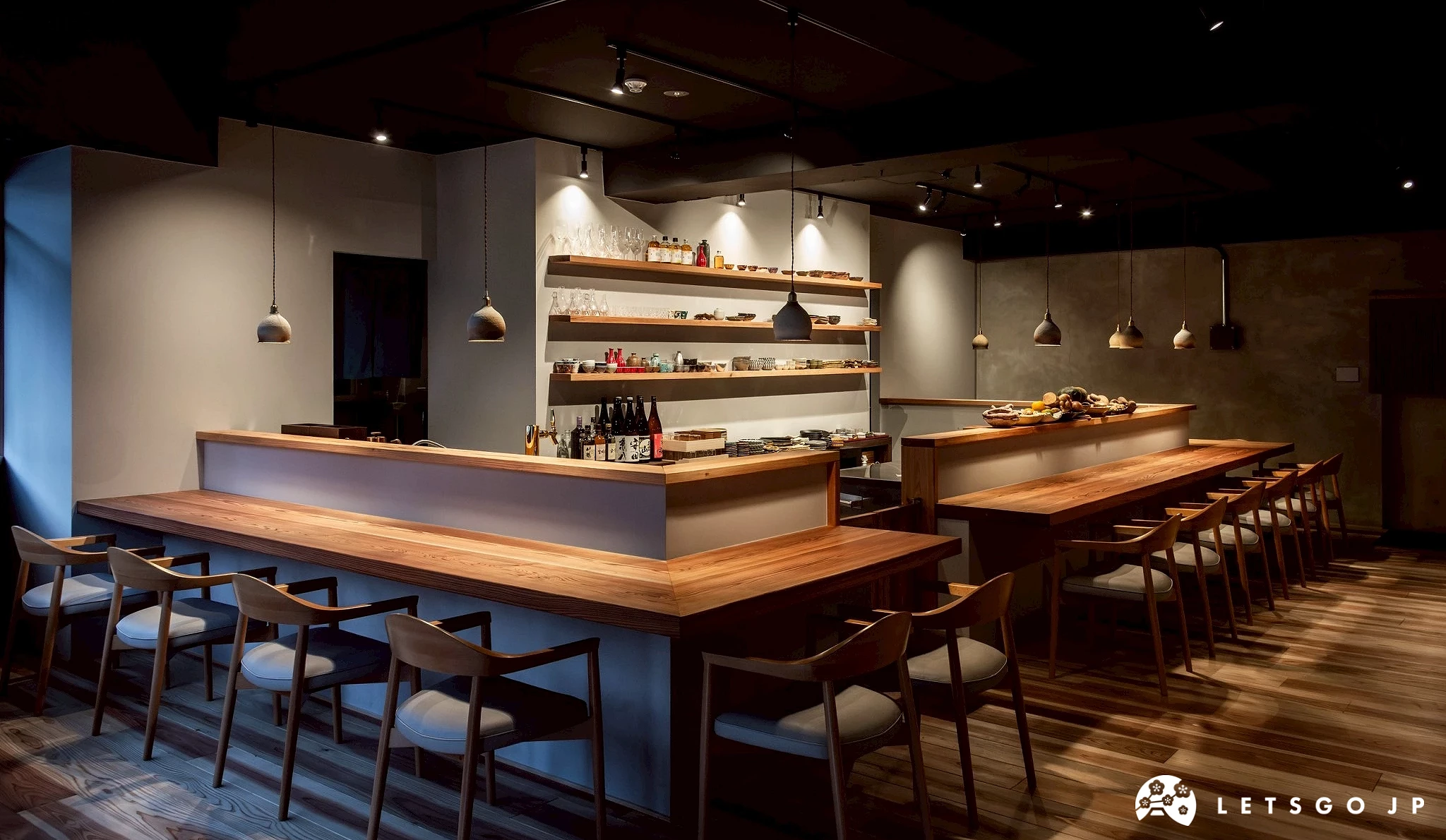 小料理吉田餐廳的內部全景。可見長形的木質吧檯,後方酒架與陳列架整齊乾淨,整體氛圍舒適雅緻。