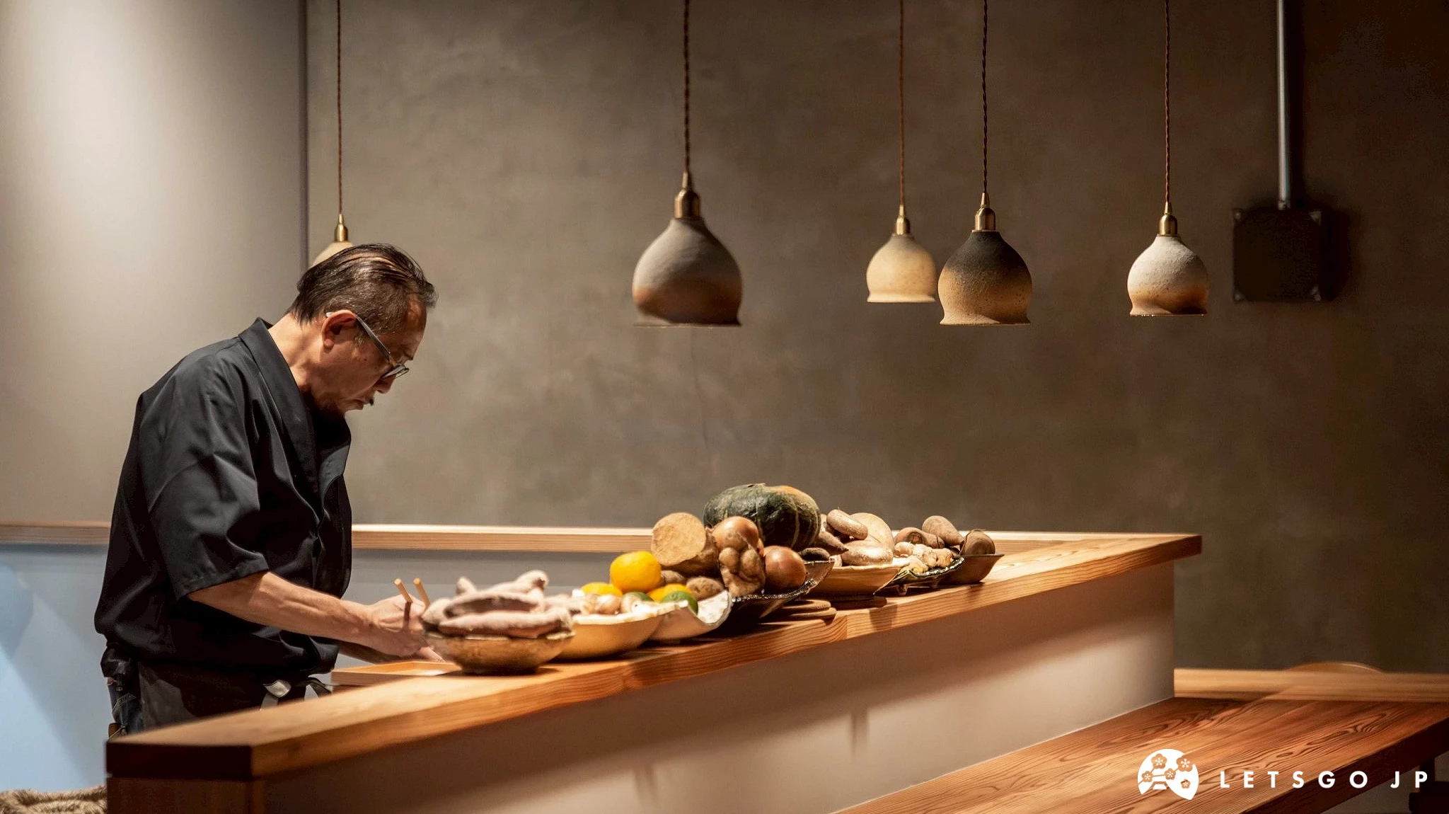 小料理吉田的吧檯區域,一位主廚正專心於料理準備工作,上方懸掛著日式造型的燈具。