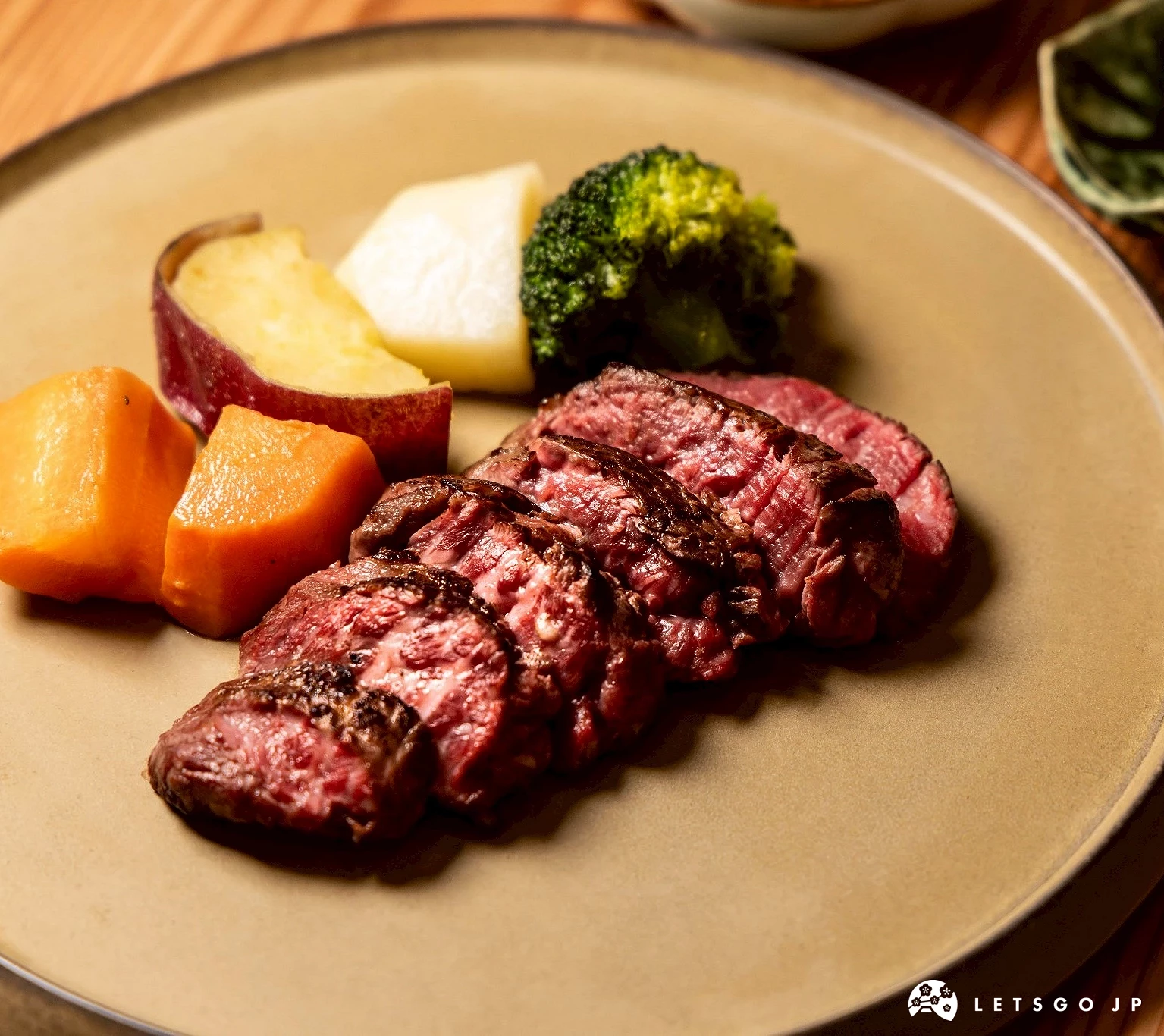 一道烤和牛排的特寫,肉片切開呈現粉嫩色澤,旁佐以季節蔬菜,盛裝於大地色系的餐盤中。