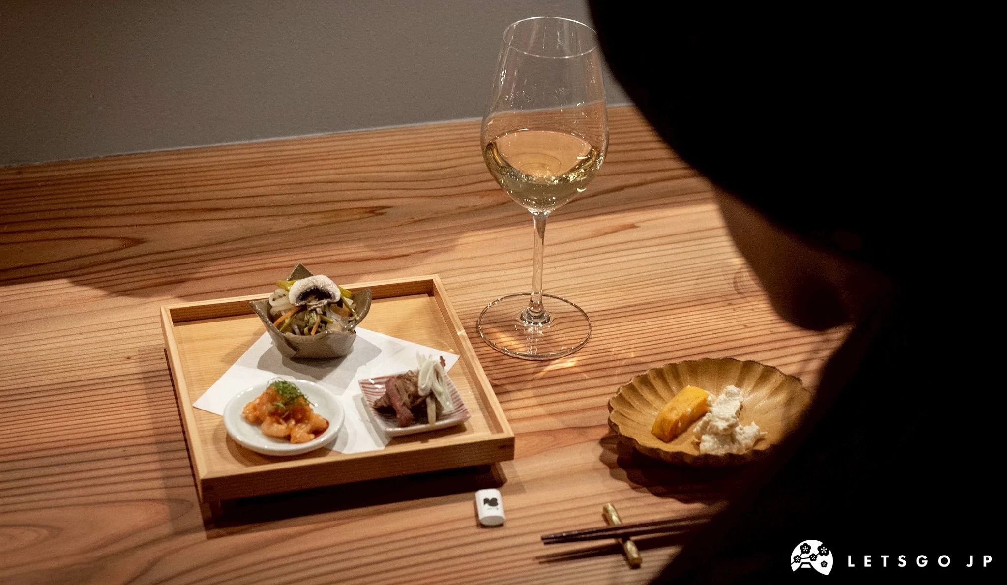 一杯白葡萄酒和數碟日式小菜(前菜/付出し),置於木質桌面上,展現精緻的餐酒搭配。