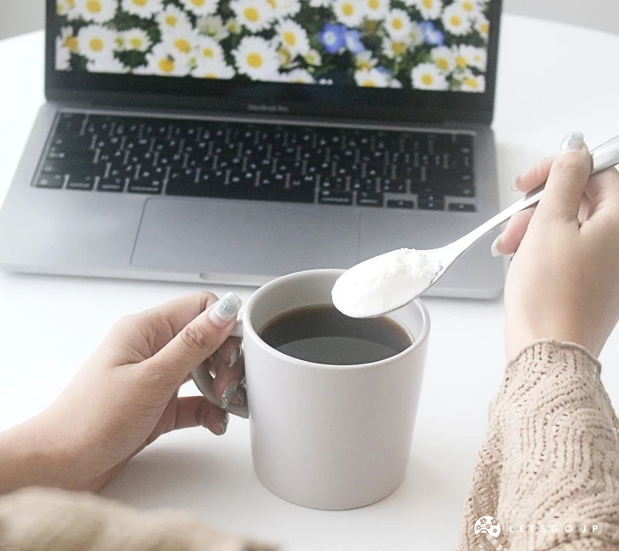 手持湯匙準備將粉末加入一杯放在筆電旁的熱咖啡