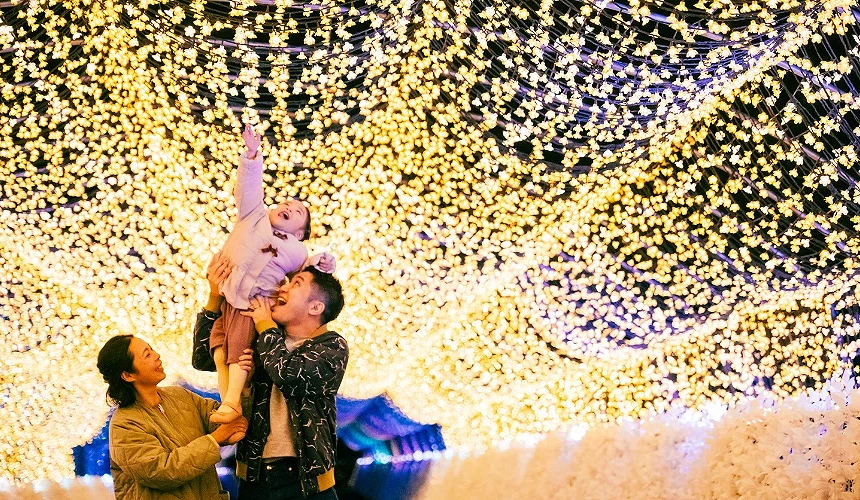 一位父亲抱着孩子站在一片温暖的金色灯饰背景下。