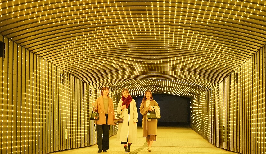 游客走在由金色灯光组成的TWINKLE TUNNEL EAST光之隧道中。