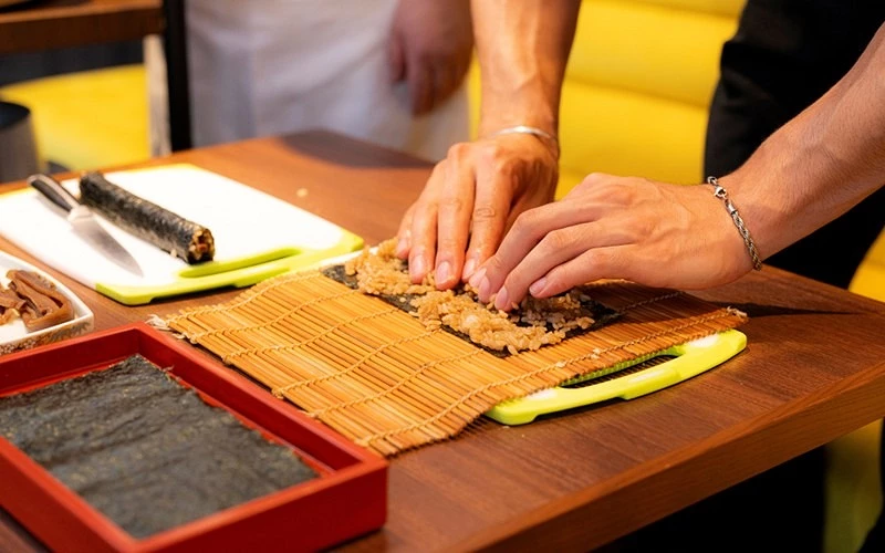 用竹簾將鋪有飯料的壽司海苔捲起