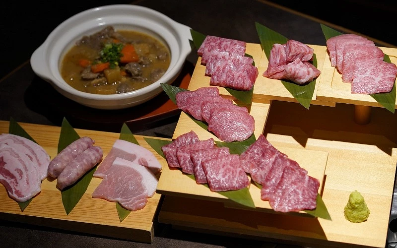 多層木盤上擺放石垣牛牛肉與豬肉片，後方有燉菜料理