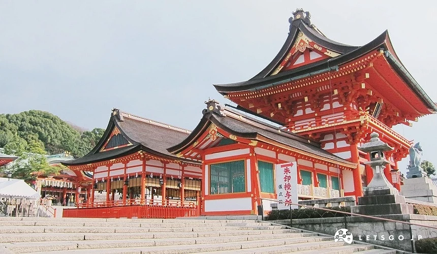 伏见稻荷大社的本殿,朱红色神社建筑与屋檐细节清晰可见,前方为石阶,背景为绿意山景