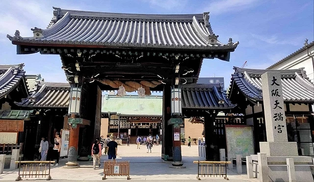大阪天滿宮的正門建築,灰瓦屋頂與木柱結構氣勢宏偉,門後可見神社境內與參拜遊客