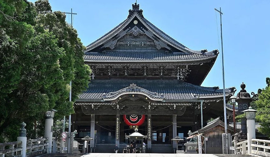 豐川稻荷本殿正面,深色木造屋舍氣勢宏偉,中間掛著大型紅黑燈籠,前方可見參拜者與石製燈籠