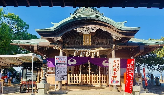 福岡鷲尾愛宕神社的拜殿正面,可見深色木造屋頂、紫色神紋幔幕與兩側告示牌,前方石地平整,環境明亮