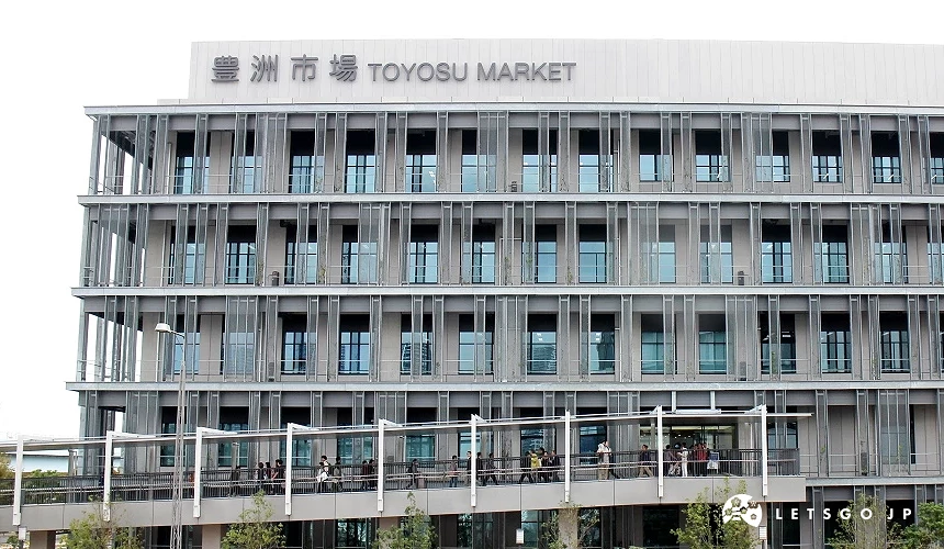 豐洲市場主棟外觀,灰色金屬結構與大片玻璃窗展現現代感設計,入口通道上可見遊客與市場工作人員往來