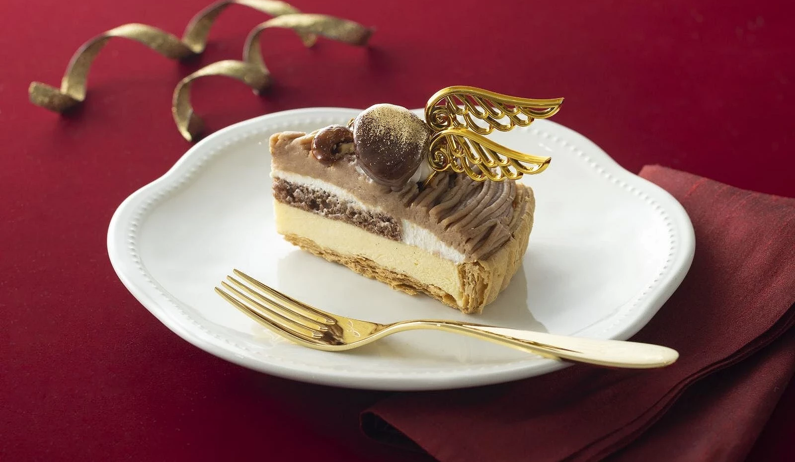 金色天使翅膀装饰的蒙布朗蛋糕,以栗子与奶油层次呈现节庆气氛,背景衬以酒红桌布与金色餐具