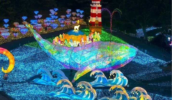 巨大的发光鲸鱼装饰漂浮于蓝色灯海之上,背上有灯塔与城堡造型,散发绚丽光彩