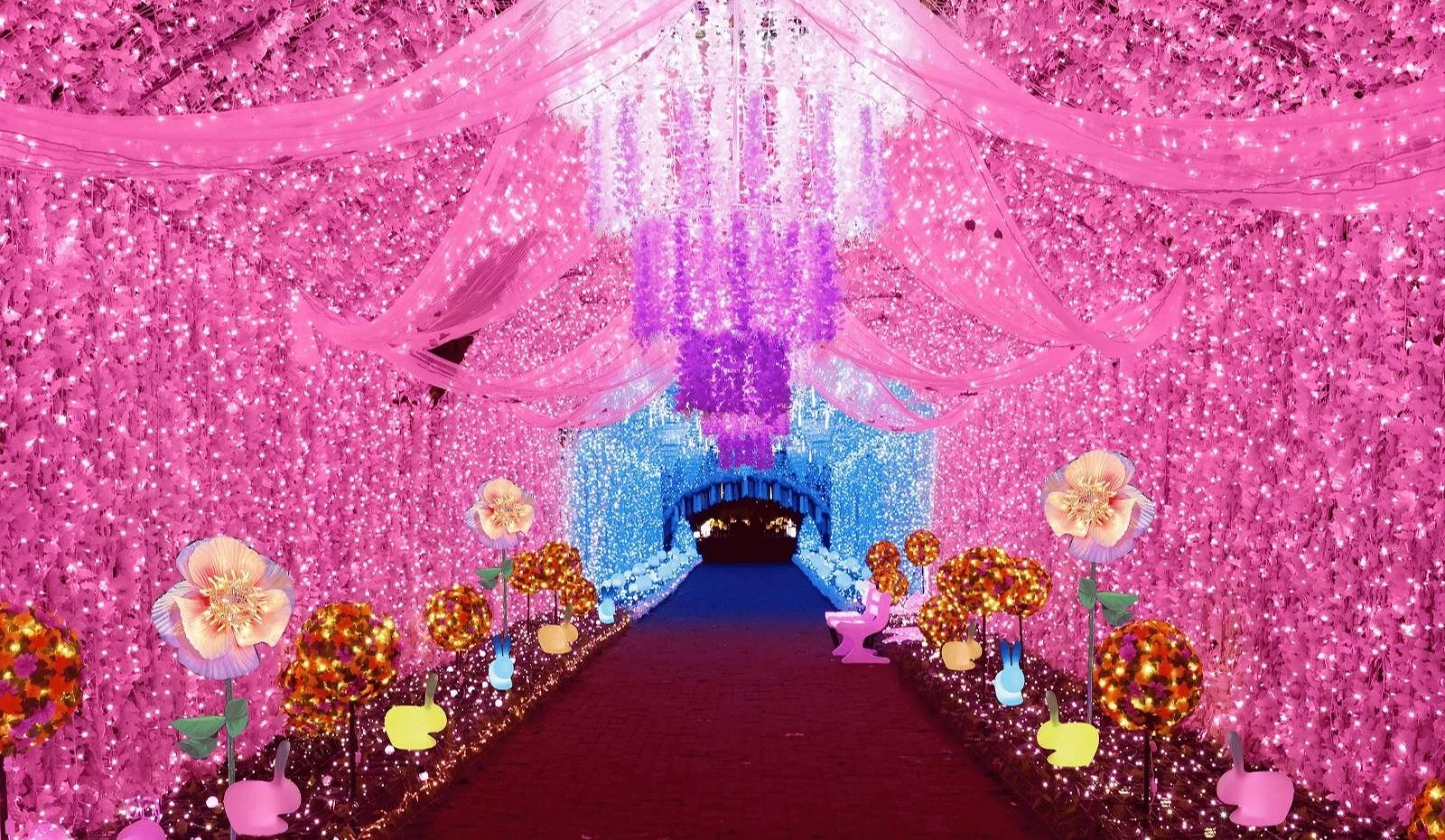 御殿场高原时之栖「光之栖所」的粉红灯海隧道,天花板挂满花卉与光幕,两侧摆放亮丽花灯与兔子造型灯饰,前方延伸至蓝色光区,营造浪漫梦幻的氛围
