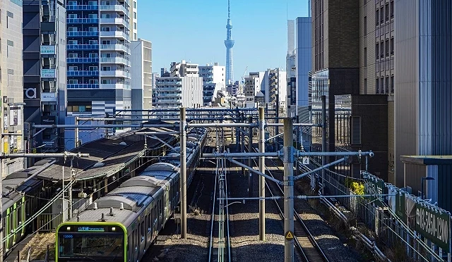 行驶中的 JR 山手线列车穿梭于东京市区铁道上,可见远方的晴空塔,呈现东京典型城市交通景象